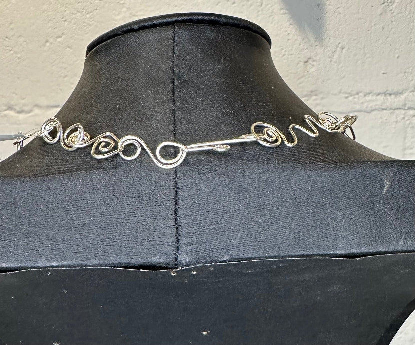 Silver wire necklace on a black mannequin against a light background