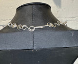 Silver wire necklace on a black mannequin against a light background
