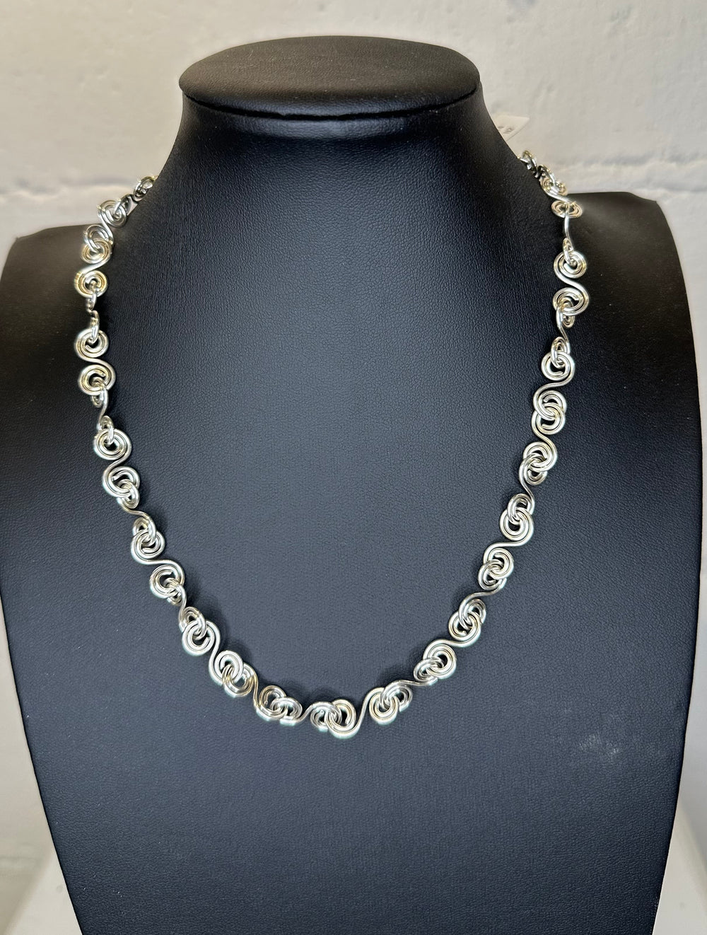 Silver necklace on a black mannequin bust against a white background