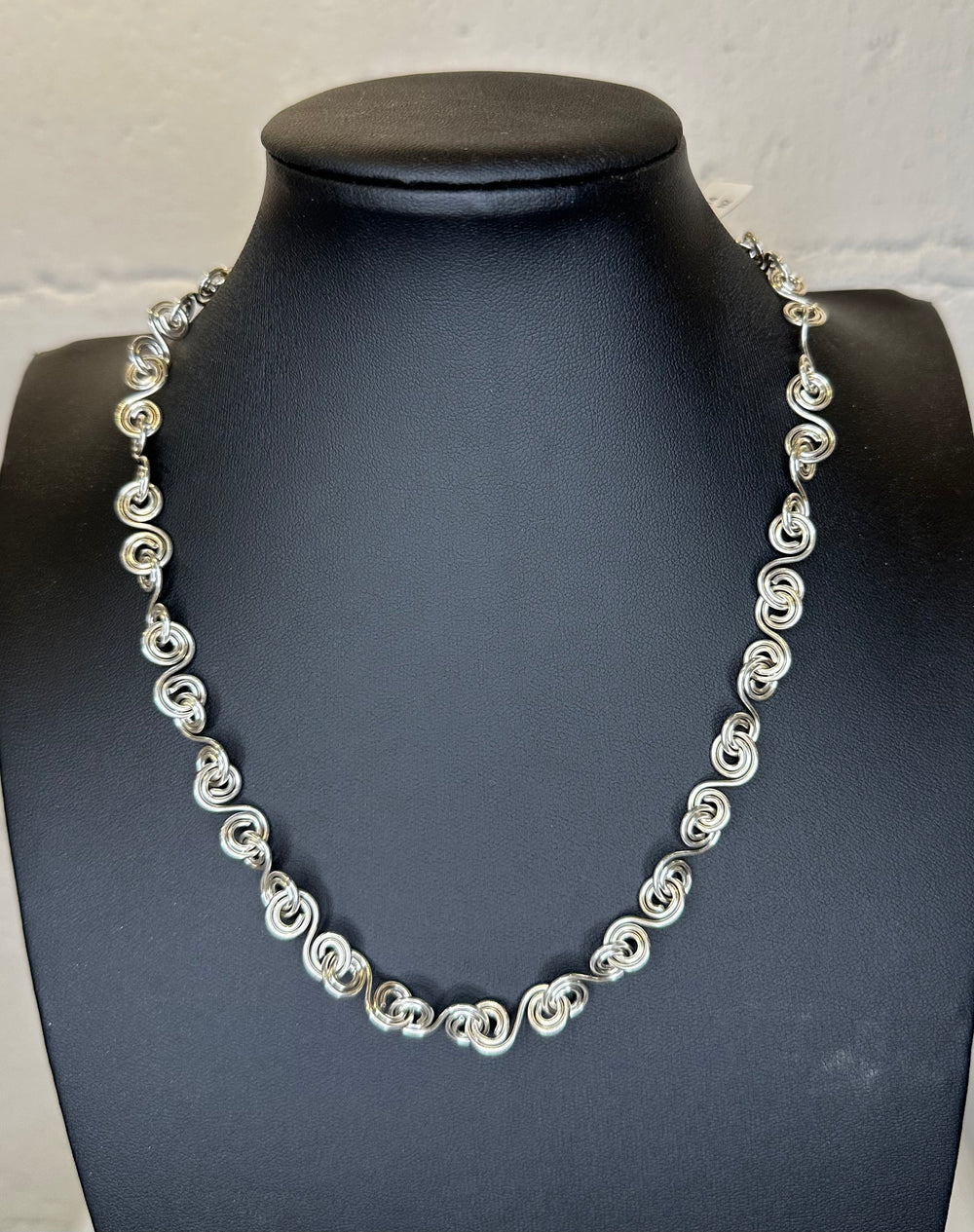 Silver necklace on a black mannequin against a white background